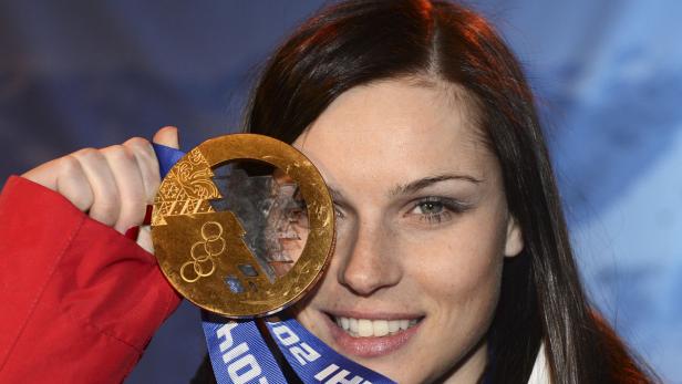 Eine Frau hält stolz eine Goldmedaille der Olympischen Winterspiele vor ihr Gesicht.