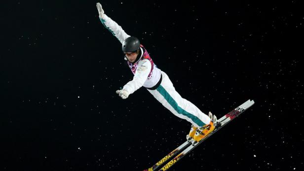 Ein Skispringer führt einen Trick in der Luft vor dunklem Nachthimmel aus.
