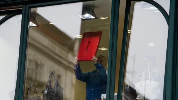 Ein Mann hält eine rote Schachtel mit der Aufschrift „Arianna“ in einem Schaufenster hoch.
