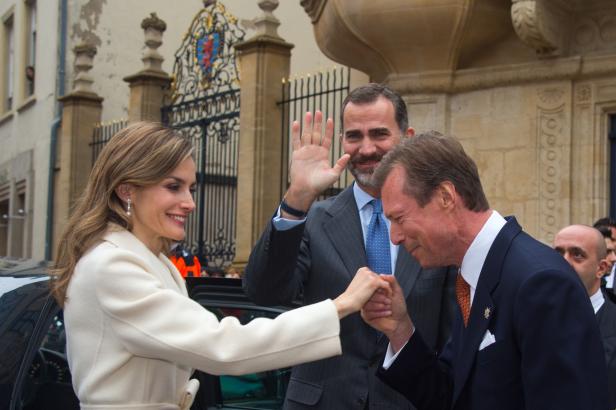 Königin Letizia wird von Großherzog Henri von Luxemburg die Hand geküsst, während König Felipe winkt.