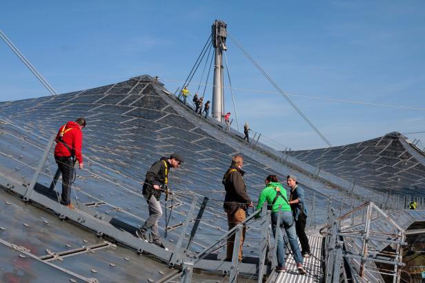 Eine Gruppe von Menschen mit Sicherheitsausrüstung auf dem Dach des Olympiaparks München.