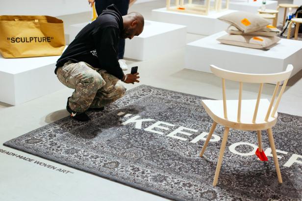 Ein Mann fotografiert einen „Keep Off“-Teppich mit einem Stuhl in einer Kunstausstellung.
