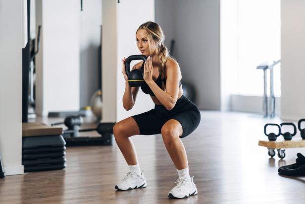 Eine Frau macht Kniebeugen mit einer Kettlebell in einem Fitnessstudio.