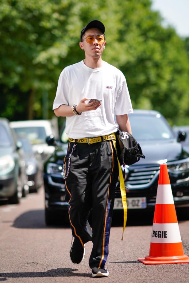 Ein Mann mit gelber Sonnenbrille und Kappe geht die Straße entlang und blickt auf sein Handy.
