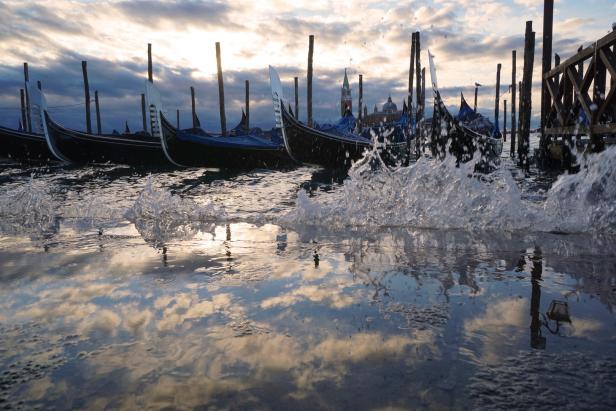 Gondeln liegen im Wasser von Venedig, das den Himmel reflektiert.