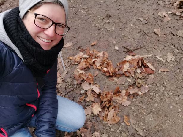 Eine Frau kniet neben einem Herz aus Herbstlaub auf dem Boden.