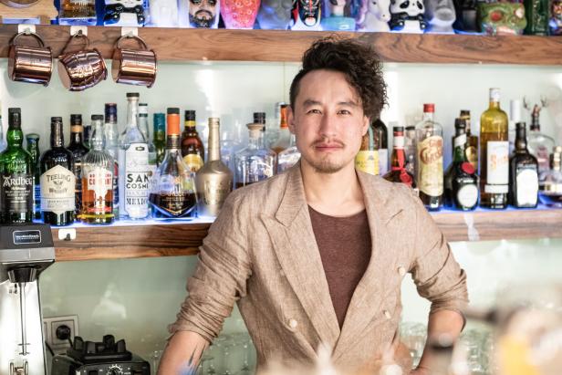 Ein Barkeeper steht vor einem Regal mit verschiedenen Spirituosenflaschen.
