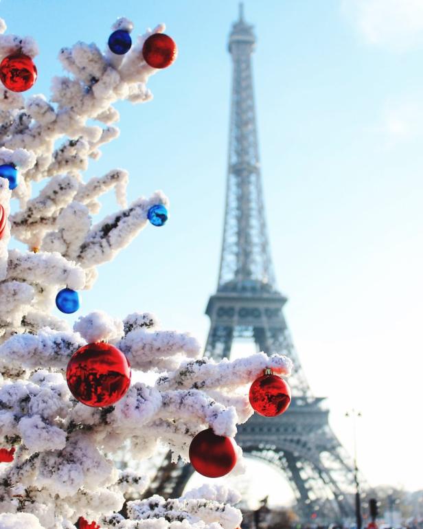 Ein schneebedeckter Weihnachtsbaum mit roten und blauen Kugeln vor dem Eiffelturm in Paris.