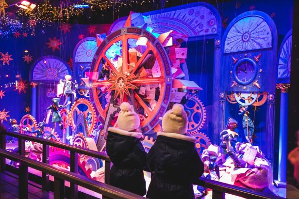 Zwei Kinder betrachten ein Schaufenster mit einem großen Rad und mechanischen Figuren.