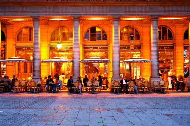Menschen sitzen abends in einem beleuchteten Straßencafé in Paris.