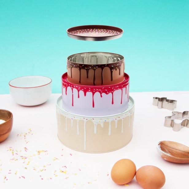 Ein gestapelter Satz von Kuchenbehältern mit Kuchendekoration und Backzutaten daneben.