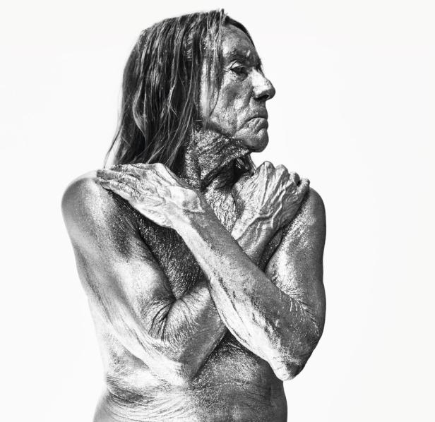 Iggy Pop, mit silberner Farbe bedeckt, posiert mit verschränkten Armen.
