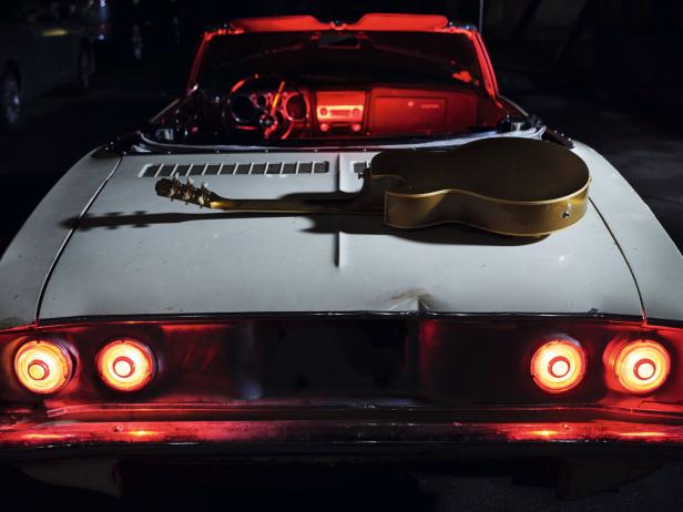 Eine goldene Gitarre liegt auf der Kofferraumhaube eines weißen Oldtimer-Cabrios.