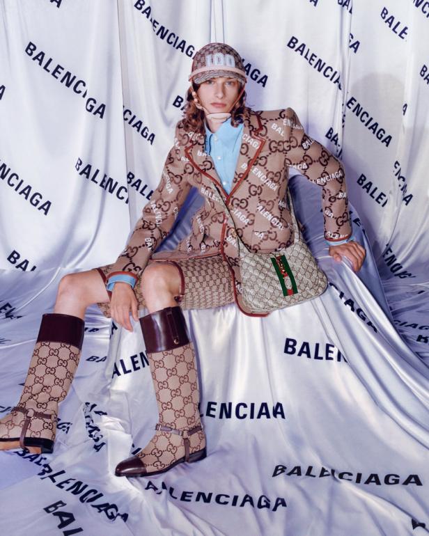 Ein Model trägt ein Gucci-Ensemble vor einem Hintergrund mit Balenciaga-Schriftzug.
