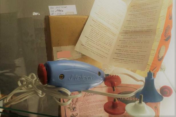 Ein blaues Massagegerät der Marke „Meteor“ aus den 1950er Jahren mit verschiedenen Aufsätzen.