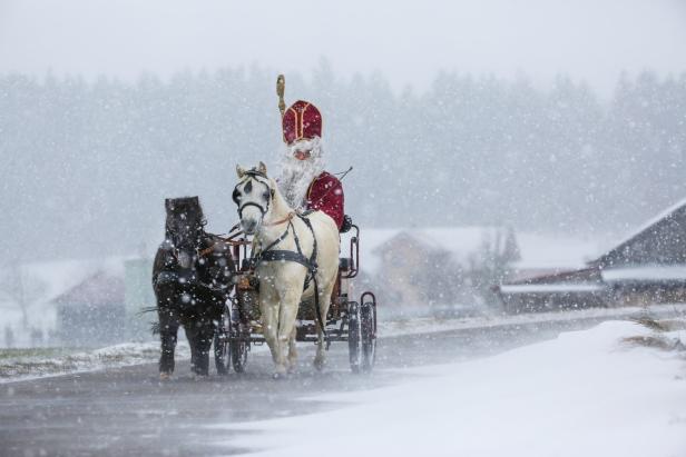 Der Nikolaus fährt mit einer Kutsche, gezogen von zwei Pferden, durch den Schnee.