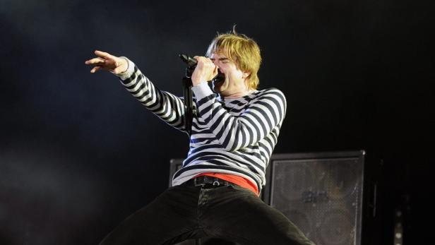 Ein Sänger mit blonden Haaren tritt auf der Bühne auf und singt in ein Mikrofon.