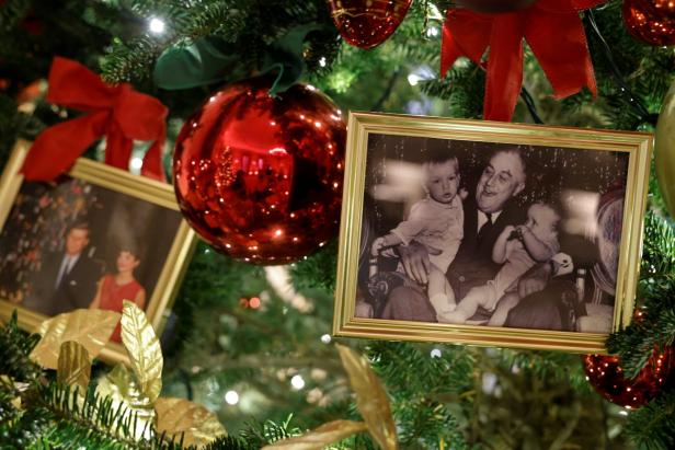 Ein Weihnachtsbaum ist mit roten Kugeln und gerahmten Fotos geschmückt.