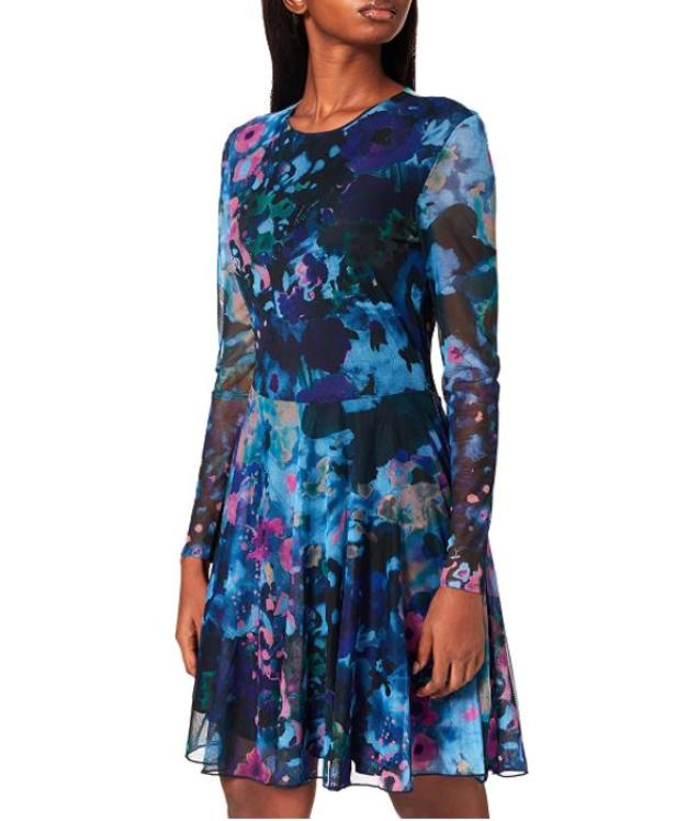 Eine Frau trägt ein blaues, gemustertes Kleid mit langen Ärmeln.