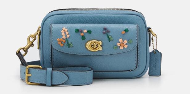 Eine blaue Coach-Umhängetasche mit floralen Stickereien auf der Vordertasche.