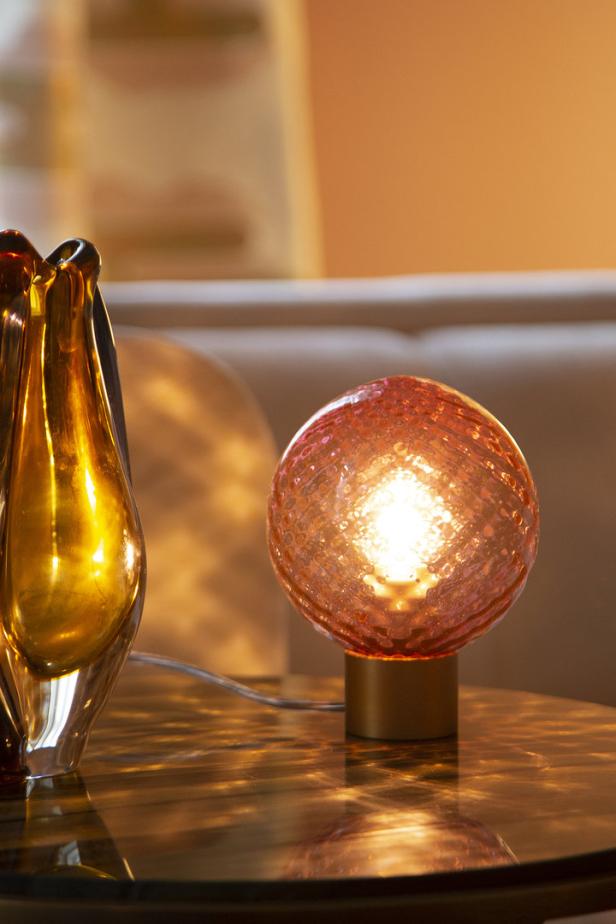 Eine orangefarbene Kugel-Lampe steht neben einer Vase auf einem Tisch.