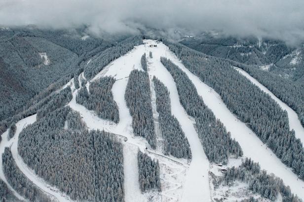 Luftaufnahme einer verschneiten Skipiste mit bewaldeten Hängen.