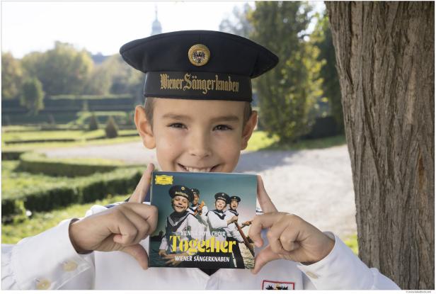 Ein Junge mit der Uniform der Wiener Sängerknaben hält die CD „Together“ in den Händen.
