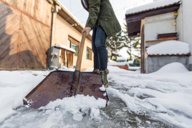 Eine Person schaufelt Schnee  vor einem Haus.