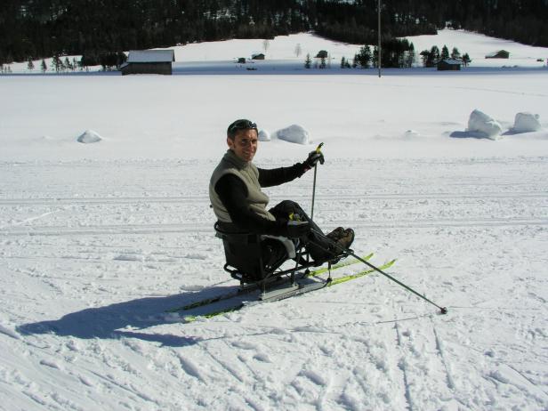 Ein Mann fährt sitzend auf Skiern durch eine verschneite Landschaft.