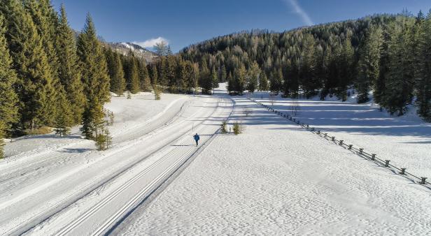 Eine Person läuft auf einer Langlaufloipe durch eine verschneite Winterlandschaft.