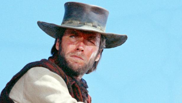 Clint Eastwood mit Bart und Cowboyhut vor blauem Himmel.