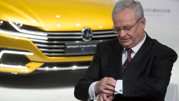 Ein Mann im Anzug blickt auf seine Armbanduhr, im Hintergrund ein gelbes Auto von Volkswagen.