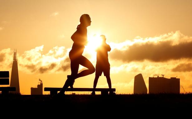 Eine Frau joggt vor einem sonnigen Himmel, während ein Kind zusieht.