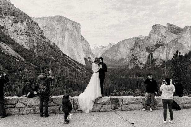 Ein Brautpaar posiert vor einer Bergkulisse im Yosemite-Nationalpark, während andere Leute Fotos machen.