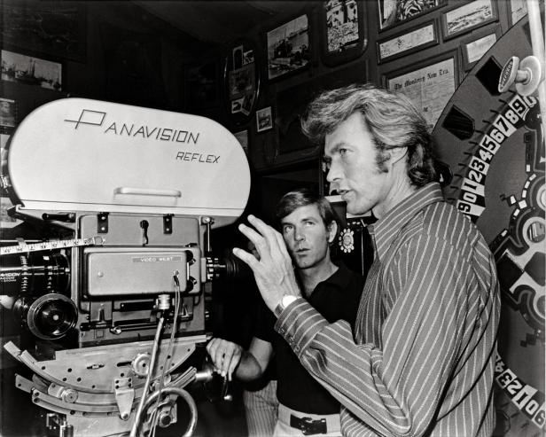 Clint Eastwood steht neben einer Panavision-Kamera und spricht mit einem Mann.