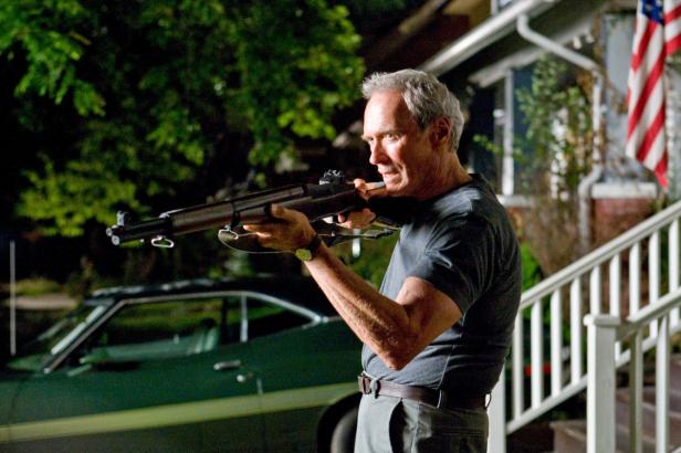 Clint Eastwood zielt mit einem Gewehr vor einem Haus.
