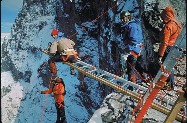 Bergsteiger überqueren eine Schlucht mit Hilfe von Leitern und Seilen.