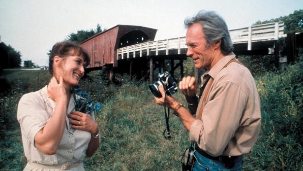 Clint Eastwood fotografiert Meryl Streep vor einer überdachten Brücke.