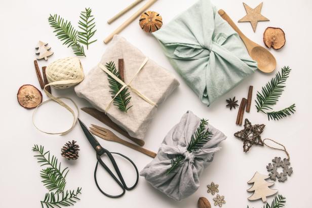 Drei Geschenke, verpackt in Stoff und dekoriert mit Tannenzweigen, liegen auf einem weißen Hintergrund.