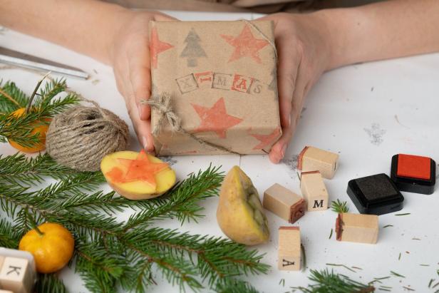 Eine Person hält ein Geschenk, das mit Kartoffelstempeln und dem Wort „X-MAS“ verziert ist.