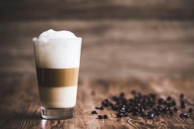 Ein Glas Caffè Latte steht neben Kaffeebohnen auf einem Holztisch.