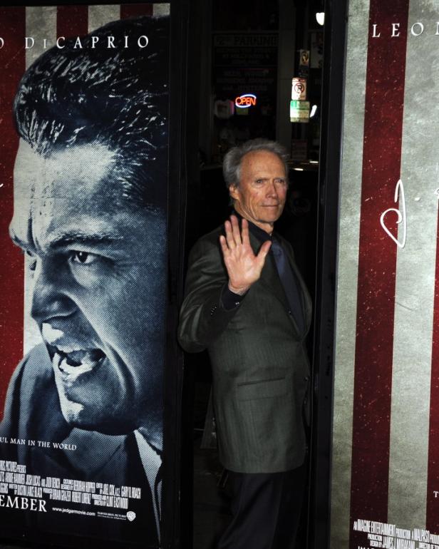 Clint Eastwood steht vor einem Filmposter mit Leonardo DiCaprio und winkt.
