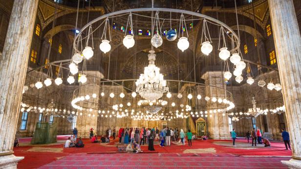 Innenansicht der Muhammad-Ali-Moschee in Kairo mit Menschen und vielen Lampen.