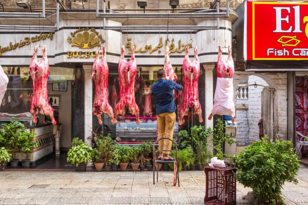 Ein Mann steht vor einer Fleischerei, an der Tierkörper hängen.
