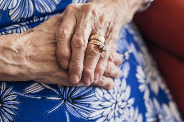 Die Hände einer älteren Frau mit Ringen liegen auf einem blau-weiß gemusterten Kleid.
