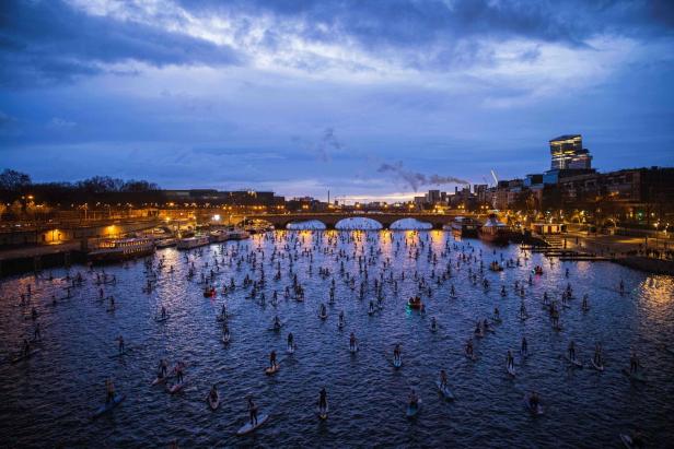 Viele Menschen paddeln bei Dämmerung auf der Seine in Paris.