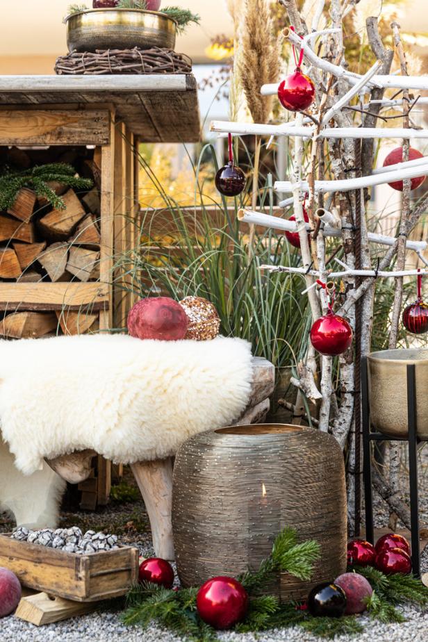 Weihnachtliche Dekoration mit roten Kugeln, einem Fell und einer Laterne im Freien.