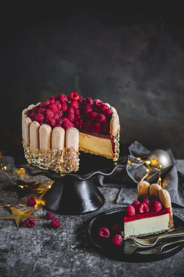 Ein Charlotte-Käsekuchen mit Himbeeren und Löffelbiskuits steht auf einem Tisch.