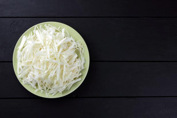 Chopped cabbage on a black background, white cabbage on a green plate, copy space, top view, vegetarian food, fresh vegetables on dark boards, black background, minimalism