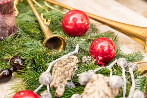 Ein Weihnachtsschmuck mit roten Kugeln, goldenen Trompeten und Tannenzweigen.